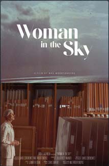 Movie poster for Woman In The Sky. Top half of the post features a cloudy sky with the movie title overlayed in white text. In the bottom half a woman, Magda Salvesen, stands in a storage room filled with the artwork of her late partner, artist John Schueler